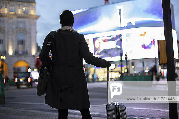 Woman with suitcase at city street corner at night  London  UK