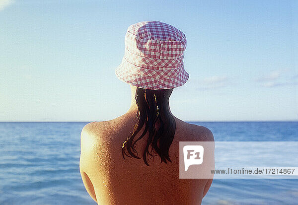 Rückansicht einer Frau mit Sonnenhut  die auf das Meer schaut