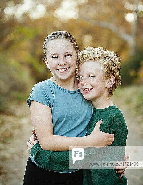 United States  California  Mission Viejo  Portrait of smiling brother (10-11) and sister (12-13) embracing in forest