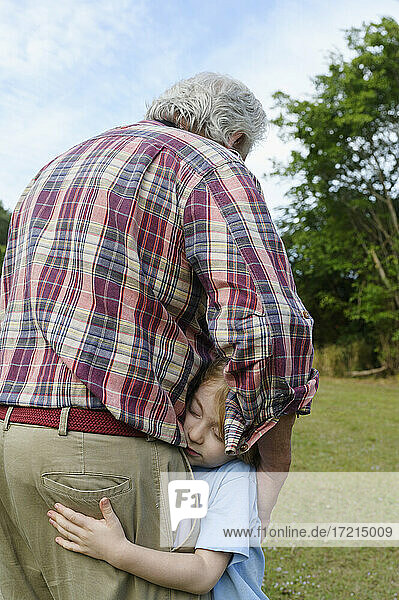 Rear view of grandfather embracing grandson (6-7) outdoors