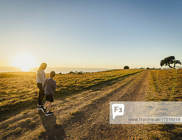 United States  California  Cambria  Rear view of mother and son (10-11) walking in landscape at sunset