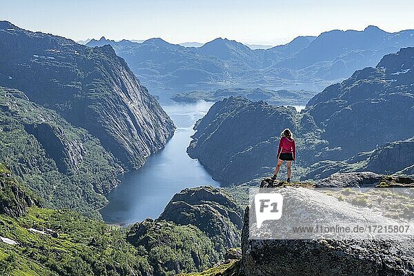 Hiker  young woman standing on rocks and looking into the distance  fjord with mountains  hiking to Trollfjord Hytta  at Trollfjord and Raftsund  Lofoten  Nordland  Norway  Europe