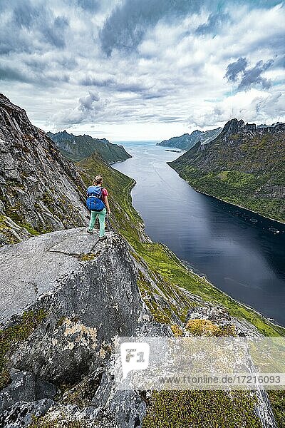 Fjord und Berge  Blick vom Berg Barden  junge Wanderin steht an einer Felsklippe  Senja  Norwegen  Europa