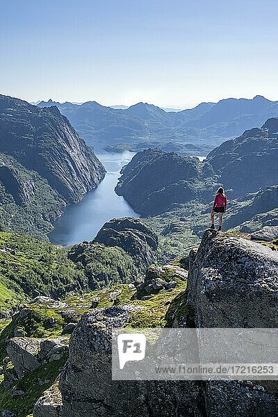 Wanderin  junge Frau steht auf Felsen und blickt in die Ferne  Fjord mit Bergen  Wanderung zur Trollfjord Hytta  am Trollfjord und Raftsund  Lofoten  Nordland  Norwegen  Europa