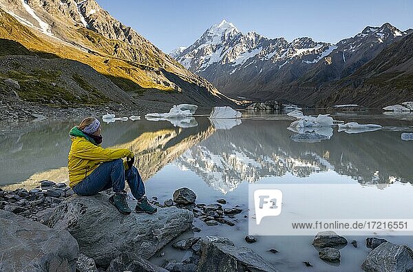 Hiker  young woman sitting on a rock  Mount Cook in morning light  Hooker Lake with reflection  sunrise  Mount Cook National Park  Southern Alps  Hooker Valley  Canterbury  South Island  New Zealand  Oceania
