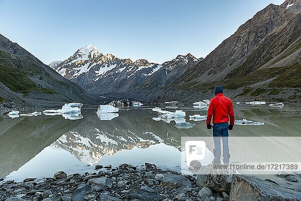 Hiker  young man standing on a rock  Mount Cook in morning light  Hooker Lake with reflection  sunrise  Mount Cook National Park  Southern Alps  Hooker Valley  Canterbury  South Island  New Zealand  Oceania