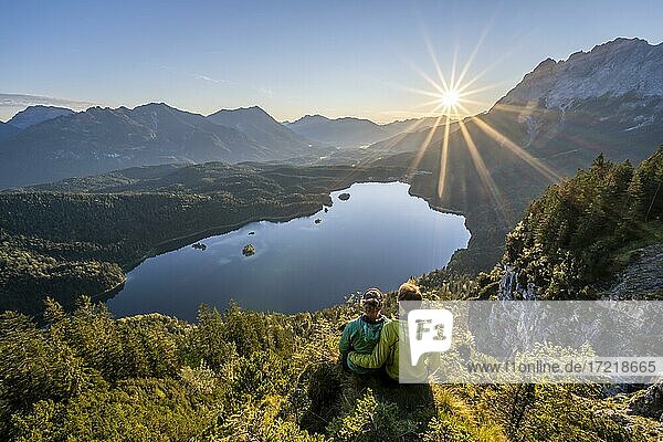 Zwei (Wanderer) blicken auf Eibsee bei Sonnenaufgang  Sonne scheint über Bayrisches Voralpenland  rechts Zugspitze  Wettersteingebirge bei Grainau  Oberbayern  Bayern  Deutschland  Europa
