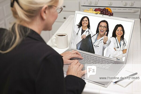 Woman sitting in kitchen using laptop viewing team of hispanic female doctors or nurses with thumbs up holding x-ray