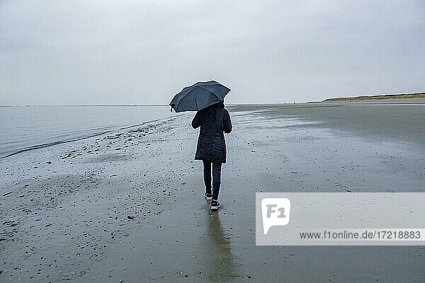 Woman with umbrella walking on the beach in rainy weather  Langeoog  East Frisian Islands  Lower Saxony  Germany  Europe