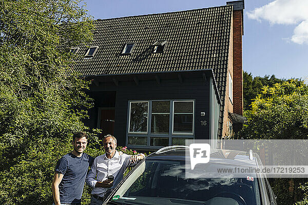 Lächelnder Vater und Sohn stehen bei einem Haus in der Nähe des Autos an einem sonnigen Tag