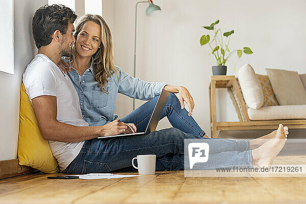 Happy couple with laptop looking at each other while sitting at home office