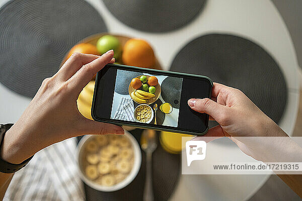 Frau  die mit ihrem Smartphone ein Foto vom Frühstück auf dem Tisch zu Hause macht