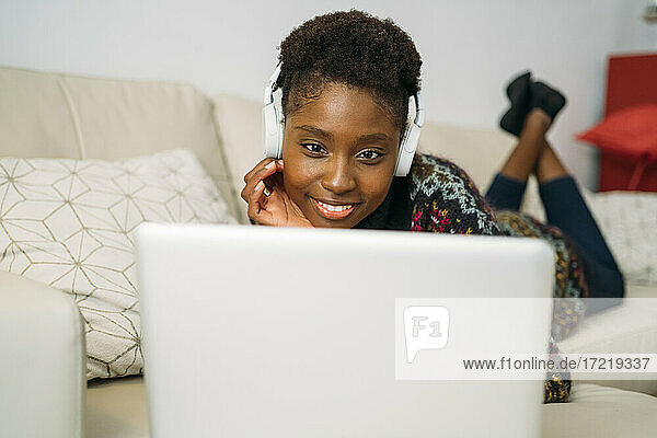 Junge Unternehmerin mit Kopfhörern bei der Telearbeit mit Laptop im Wohnzimmer