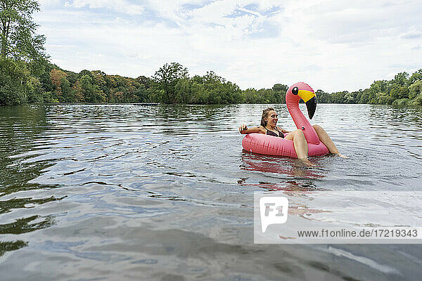 Junge Frau schwimmt auf einem See in einem rosa Flamingo schwimmenden Reifen