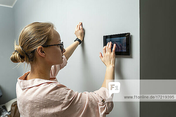 Young woman using home automation device while standing by wall at home