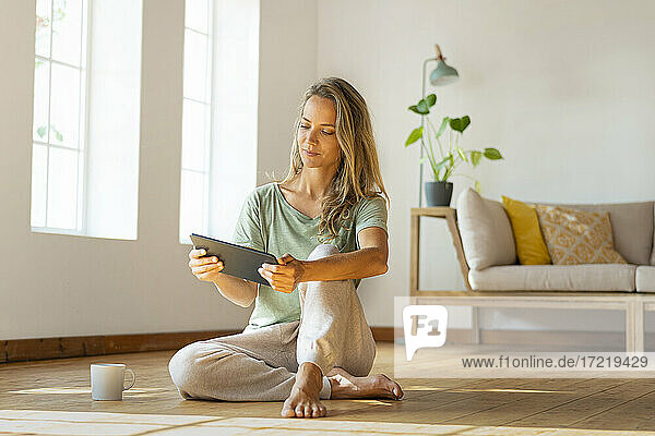 Woman in loungewear looking at digital tablet while sitting in living room