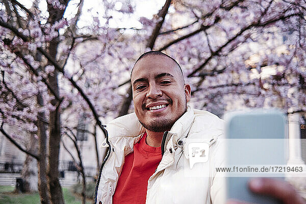 Gut aussehender lächelnder Mann  der ein Selfie in einem öffentlichen Park macht