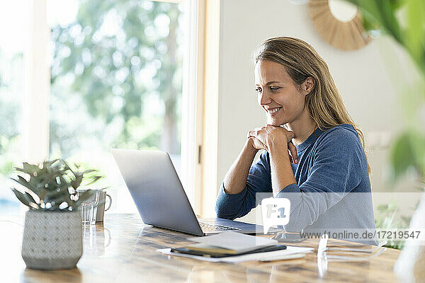 Smiling female entrepreneur looking at laptop while sitting at table