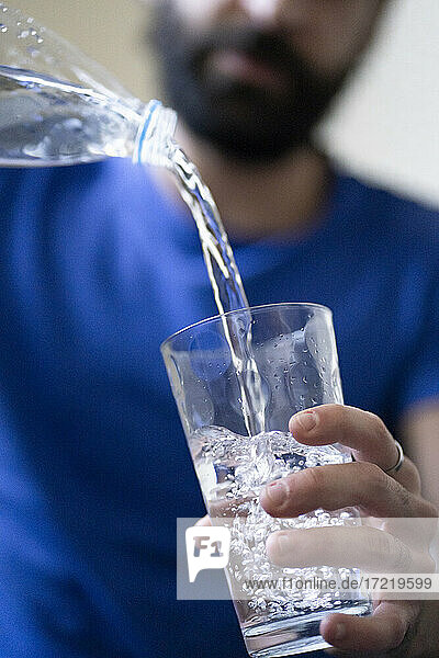 Junger Mann gießt Wasser in ein Glas