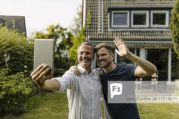 Lächelnder Vater und Sohn unterhalten sich während eines Videoanrufs über ein digitales Tablet  während sie im Hinterhof stehen