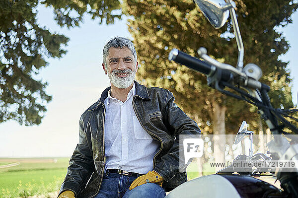 Lächelnder Mann in Bikerjacke auf einem Motorrad sitzend