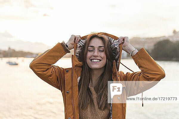 Spanien  Kantabrien  San Vicente de la Barquera  Lächelnde junge Frau genießt die Meeresküste bei Sonnenuntergang