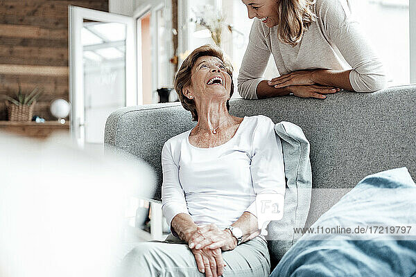 Lachende Großmutter  die ihre Enkelin an das Sofa lehnt