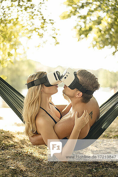 Paar entspannt sich in Hängematte am See  küsst sich  benutzt VR-Brille