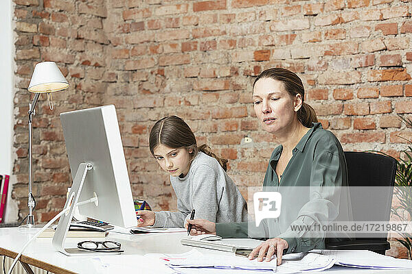 Female professional working by daughter studying at desk