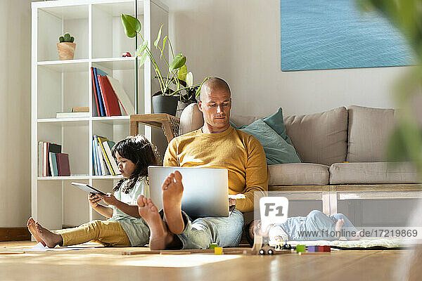 Vater arbeitet am Laptop  während er bei seinen Töchtern zu Hause sitzt