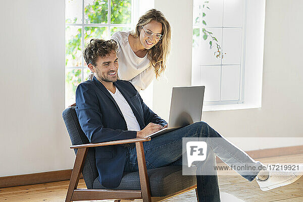 Mann benutzt Laptop  während er bei seiner Freundin zu Hause auf dem Stuhl sitzt