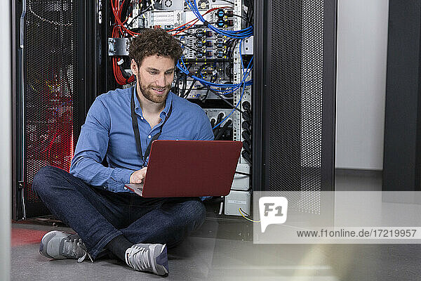 Male IT engineer working on laptop in front of rack in data center