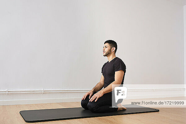 Man kneeling on mat by wall in exercise room