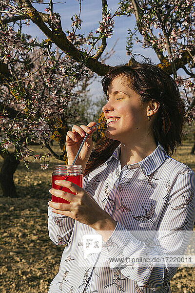 Lächelnde Frau mit Erdbeer-Soda an Mandelbäumen