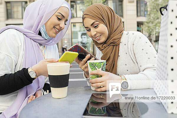 Freundinnen mit wiederverwendbaren Bechern auf dem Tisch und einem Smartphone in einem Straßencafé in der Stadt