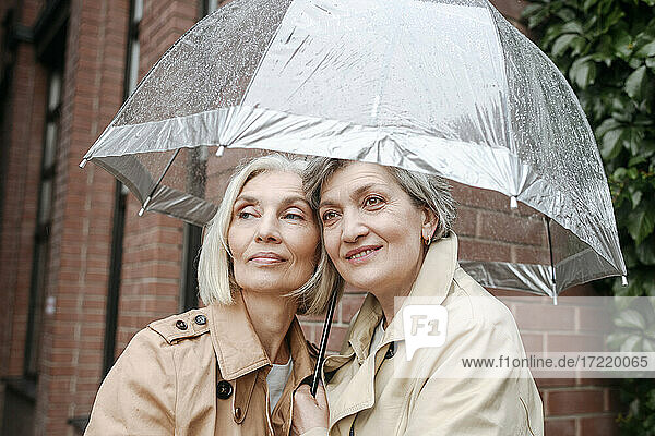 Smiling female friends under umbrella on rainy day