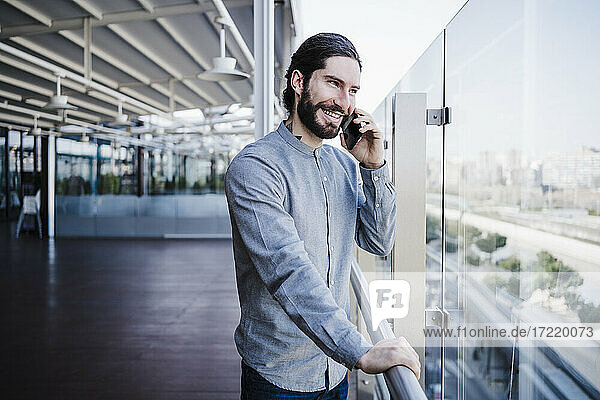 Creative businessman talking on mobile phone while looking though glass in office