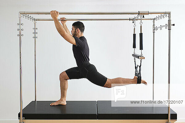 Mid adult male athlete practicing pilates on trapeze table in exercise room
