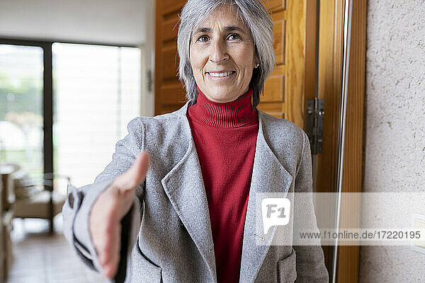 Smiling mature woman offering handshake at doorway