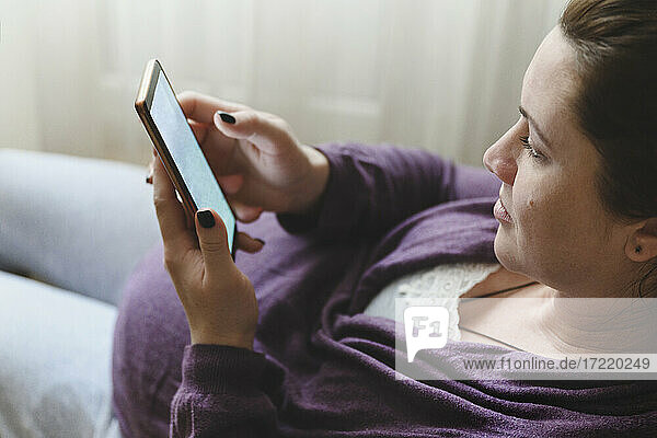 Schwangere Frau benutzt Mobiltelefon  während sie zu Hause liegt