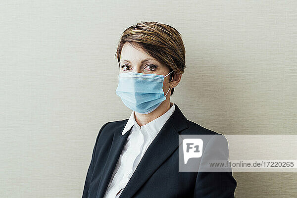 Unternehmerin mit Gesichtsschutzmaske vor beiger Wand im Büro