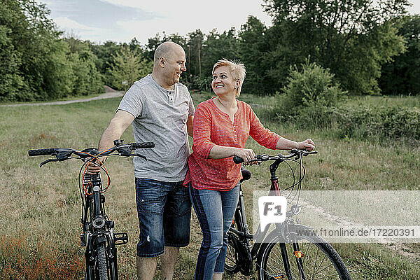 Smiling mature couple with bicycle at field