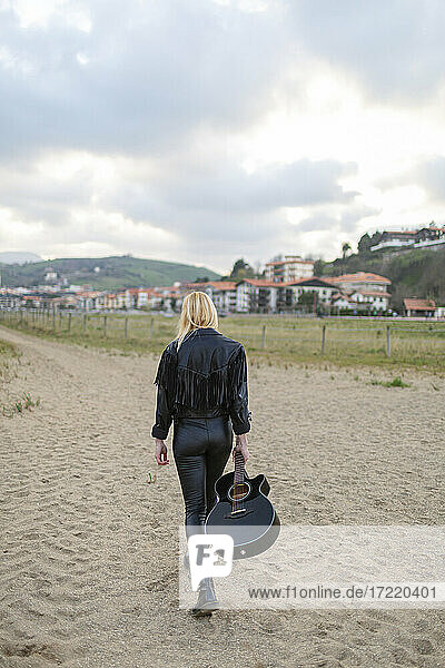 Young woman guitarist walking on sand carrying guitar