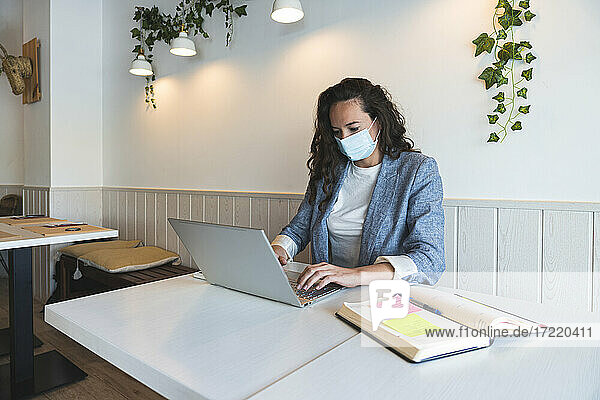 Freiberufliche Mitarbeiterin mit Laptop in einem Café während der COVID-19