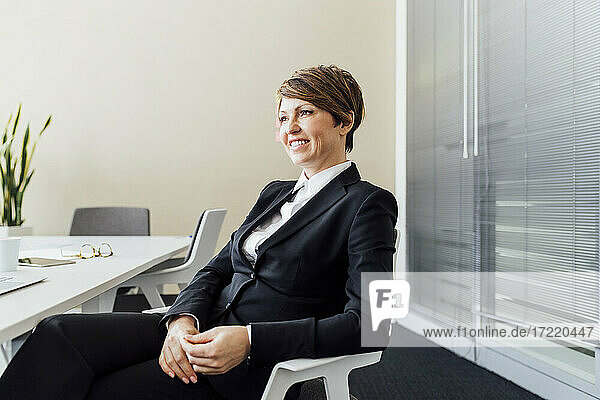 Lächelnde weibliche Business Professional Tag träumen  während auf Stuhl im Büro sitzen