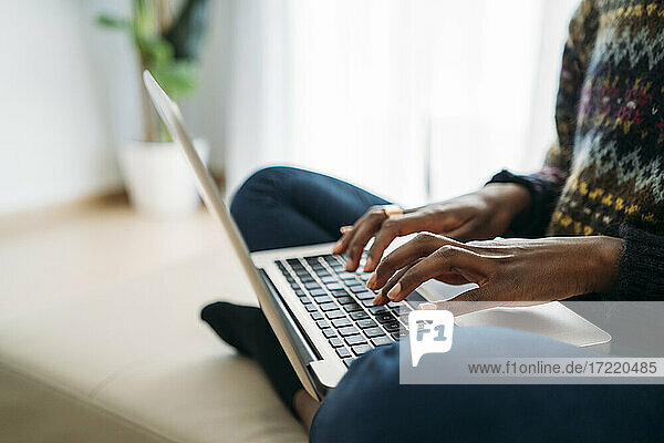 Weibliche Fachkraft tippt auf einem Laptop  während sie im Wohnzimmer zu Hause arbeitet