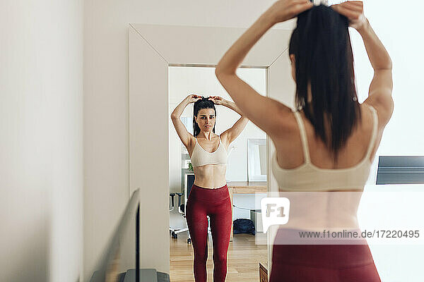 Frau bindet Haare  während sie zu Hause in den Spiegel schaut