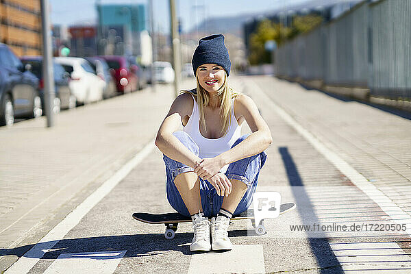Lächelnde schöne Frau sitzt auf Skateboard während sonnigen Tag