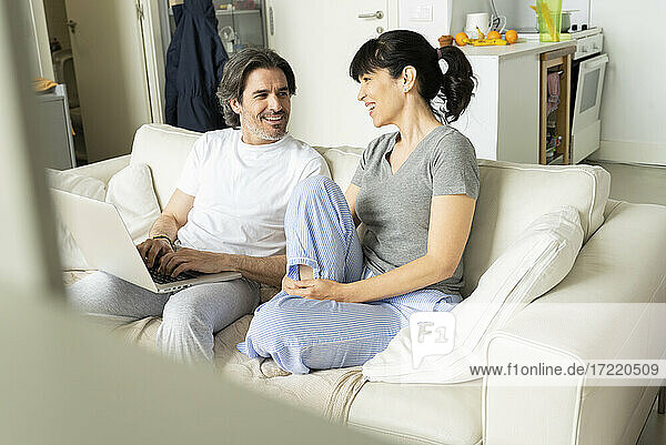 Mann mit Laptop im Gespräch mit Frau auf dem Sofa im Wohnzimmer zu Hause