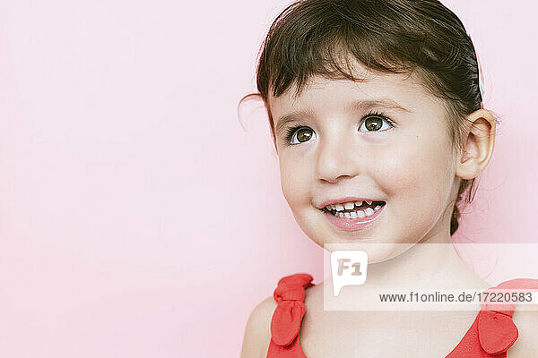 Portrait of smiling little girl in front of pink background looking up